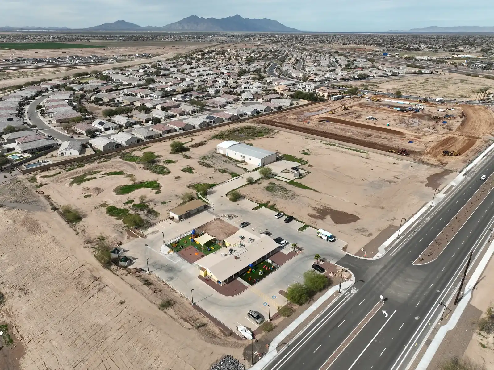 Aerial view of a development site with graded pads beside an existing neighborhood in Maricopa, Arizona
